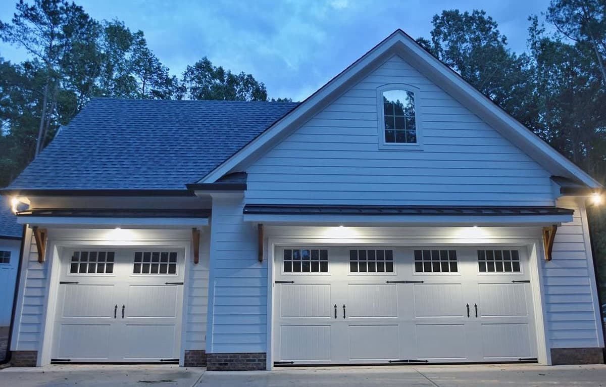 Two white carriage-style garage doors on a detached garage, lit from above at dusk.